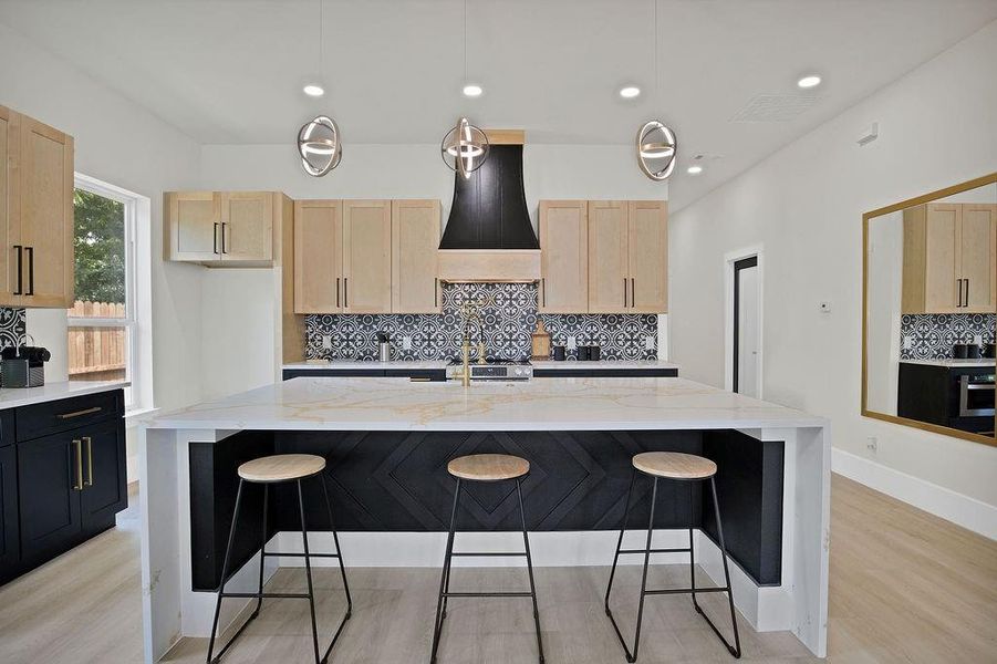 Kitchen featuring pendant lighting, light hardwood / wood-style flooring, an island with sink, light stone countertops, and decorative backsplash