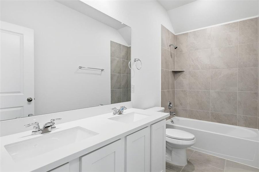 Bathroom featuring a dual vanity with white cabinetry and integrated sinks, chrome fixtures, a full-width wall mirror, a bathtub with a tiled surround, and floor-level tiling