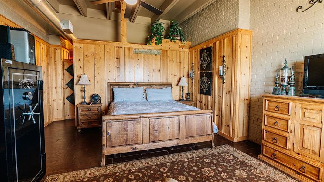 Bedroom with dark wood-type flooring, brick wall, and beamed ceiling