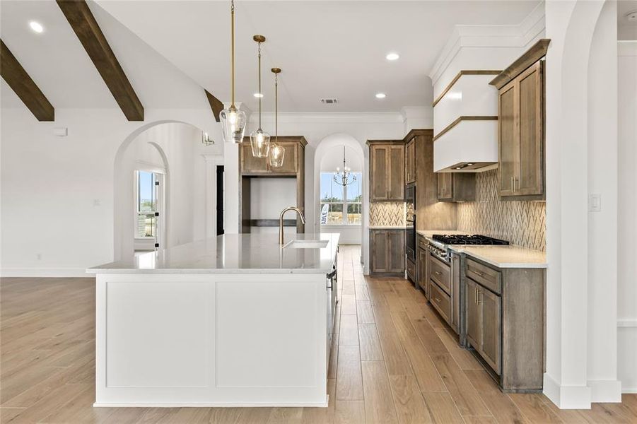 Open-concept kitchen featuring an oversized island, wood-finish flooring, vaulted ceilings with exposed beams, custom cabinetry, and a tile backsplash