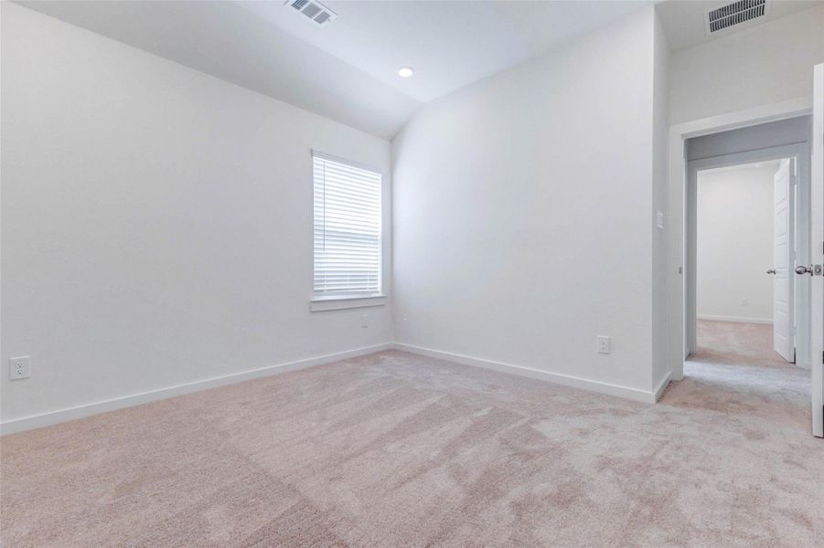 Bright secondary bedroom with soft carpet, high ceiling, recessed lighting, window with blinds, and neutral walls. The open floor area allows flexible furniture placement, while the adjoining doorway connects easily to the rest of the bedroom wing. This room is ideal for a guest suite, child’s bedroom, nursery, home office, or quiet hobby space.