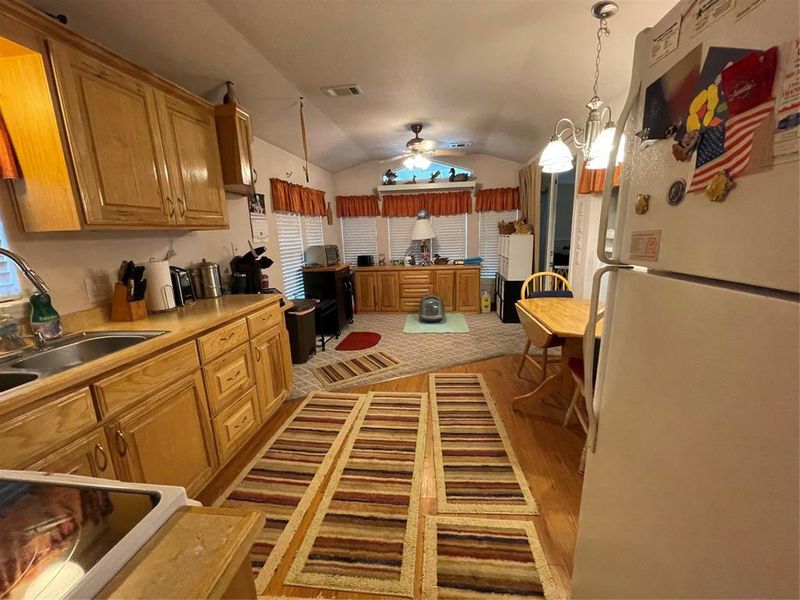 Kitchen featuring vaulted ceiling, ceiling fan with notable chandelier, light hardwood / wood-style flooring, sink, and fridge Kitchen featuring vaulted ceiling, ceiling fan with notable chandelier, light hardwood / wood-style flooring, sink, and fridge