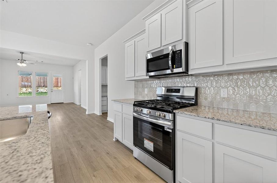Kitchen with stainless steel appliances, white cabinetry, and light stone counters