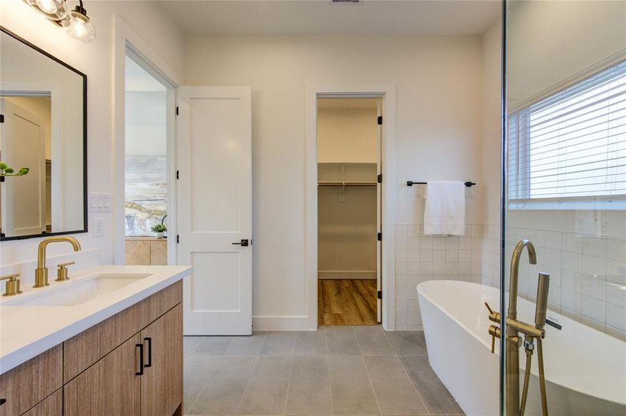 This primary bathroom feels like a spa with designer tile work, elegant champagne bronze fixtures, large soaking tub and walk-in shower, double vanity, and separated toilet room.