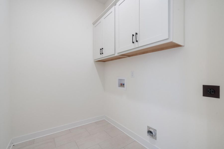 White wall-mounted cabinetry with matte black hardware, recessed water supply box, electric dryer outlet, and rectangular tile flooring White wall-mounted cabinetry with matte black hardware, recessed water supply box, electric dryer outlet, and rectangular tile flooring