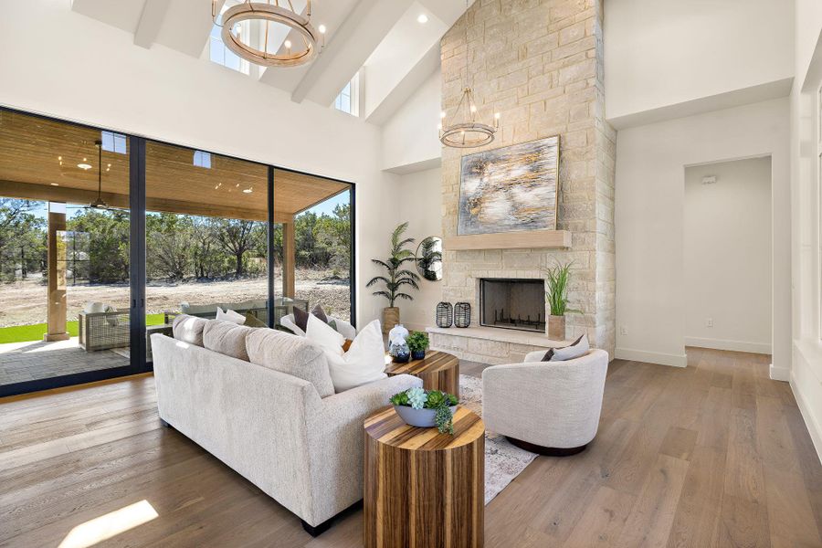 Living room featuring a notable chandelier, a high ceiling, a stone fireplace, wood finished floors, and baseboards