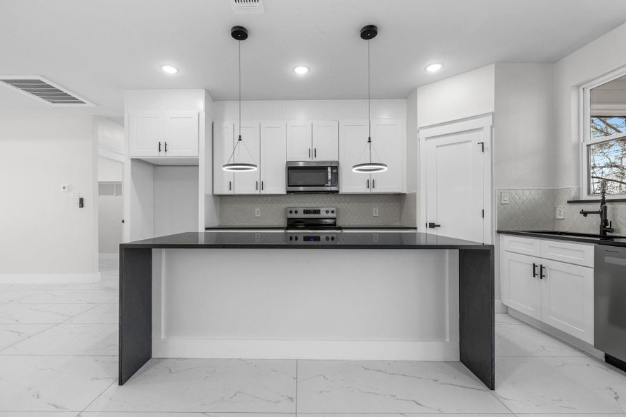 Kitchen featuring white cabinets, stainless steel appliances, and pendant lighting