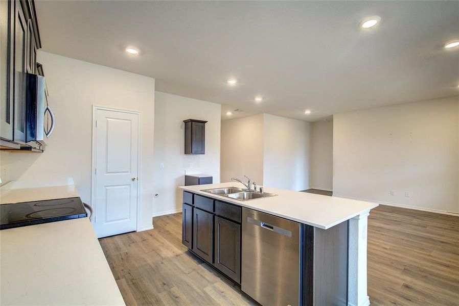 Kitchen with appliances with stainless steel finishes, a kitchen island with sink, light wood finished floors, recessed lighting, and dark brown cabinetry