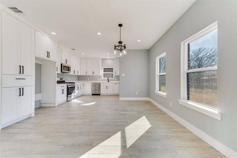 Kitchen featuring white cabinetry, appliances with stainless steel finishes, decorative light fixtures, and plenty of natural light