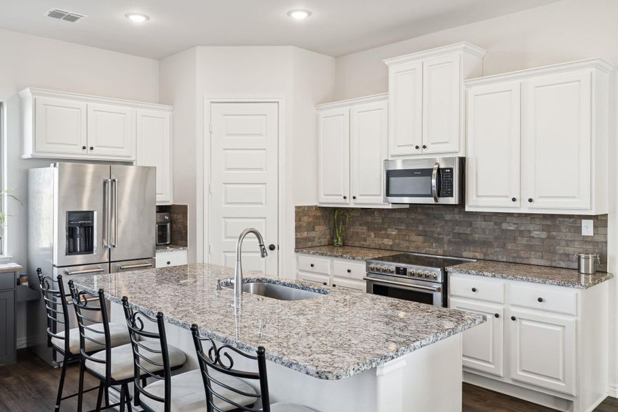 Kitchen with tasteful backsplash, light stone countertops, appliances with stainless steel finishes, white cabinetry, and dark wood-type flooring Kitchen with tasteful backsplash, light stone countertops, appliances with stainless steel finishes, white cabinetry, and dark wood-type flooring