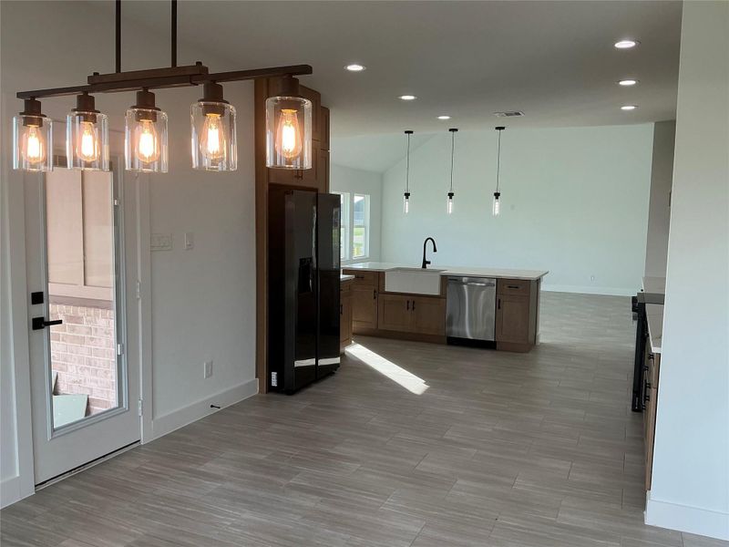 This photo showcases a modern kitchen and dining area with an open floor plan. It features stylish pendant lighting, a central island with a farmhouse sink, stainless steel appliances, and sleek tile flooring, all under recessed lighting for a bright and inviting space.