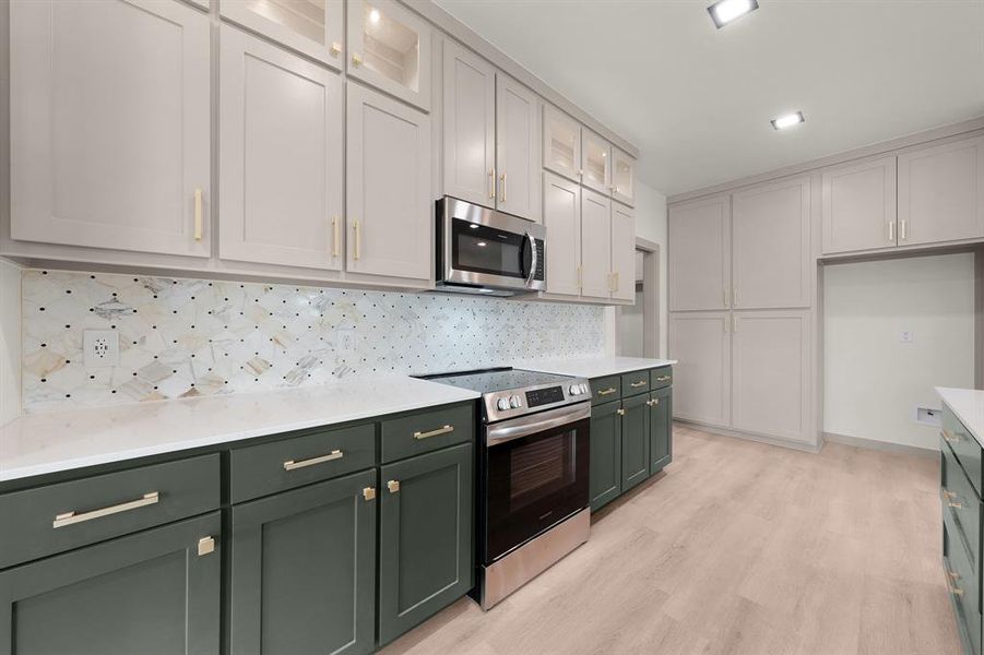 Kitchen featuring green cabinetry, light countertops, light wood-style flooring, stainless steel appliances, and tasteful backsplash