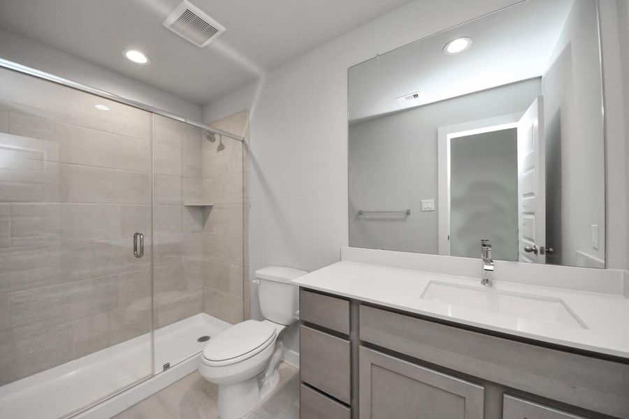 Secondary bath features tile flooring, walk-in shower with tile surround, light stained wood cabinets, beautiful light countertop.