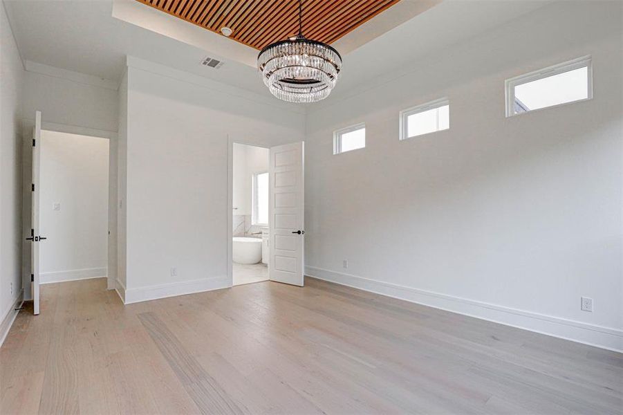 Unfurnished bedroom featuring a notable chandelier, wood ceiling, light wood-type flooring, and a raised ceiling