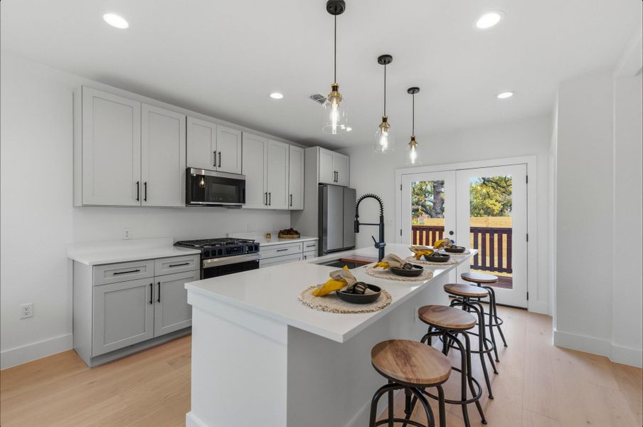 Kitchen with a breakfast bar, a center island with sink, appliances with stainless steel finishes, hanging light fixtures, and recessed lighting