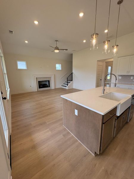 Open-concept living area featuring wood-finish flooring, a contemporary fireplace with a classic mantel, and a kitchen island with a farmhouse sink
