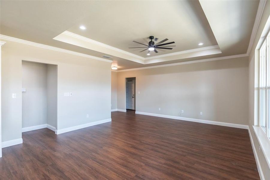 Spacious room featuring wood-finish flooring, a tray ceiling with recessed lighting and ceiling fan, and large windows with white trim