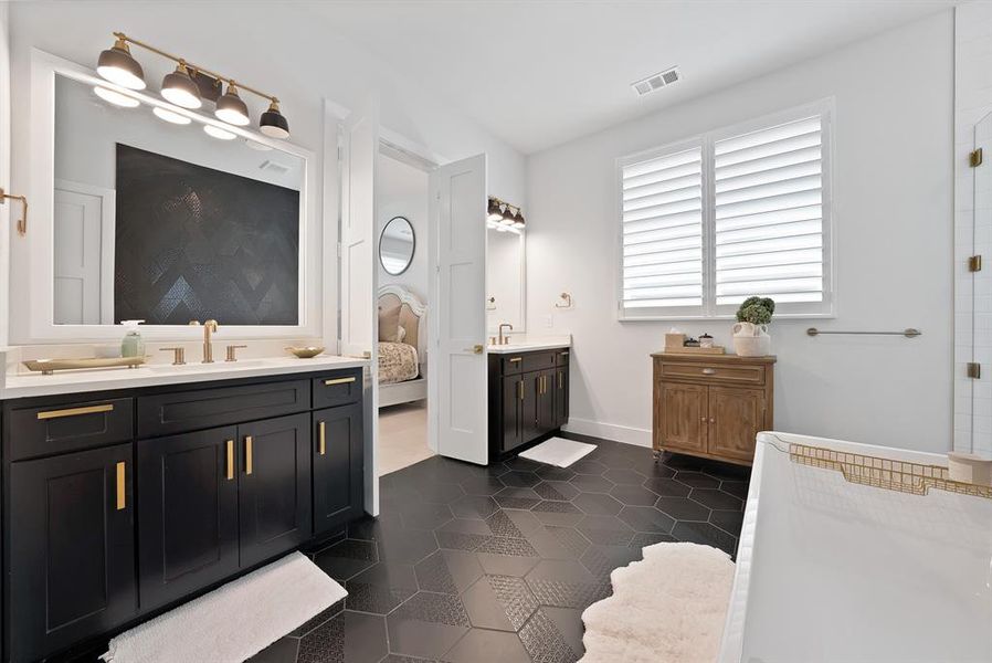 Bathroom featuring dual black vanities with gold hardware, white countertops, and a full-width mirror Bathroom featuring dual black vanities with gold hardware, white countertops, and a full-width mirror