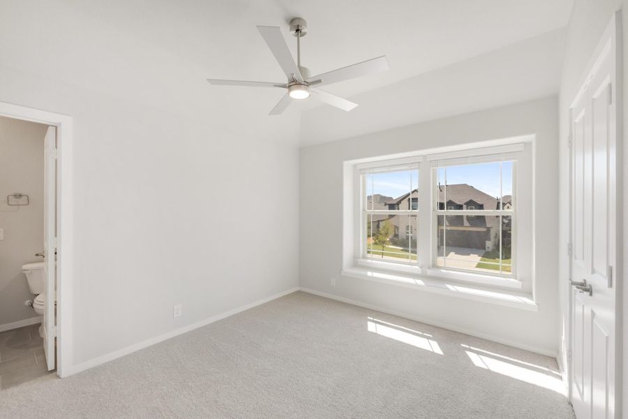 Empty bedroom with vaulted ceiling, ceiling fan, carpet flooring, and attached bathroom visible through open door. Empty bedroom with vaulted ceiling, ceiling fan, carpet flooring, and attached bathroom visible through open door.