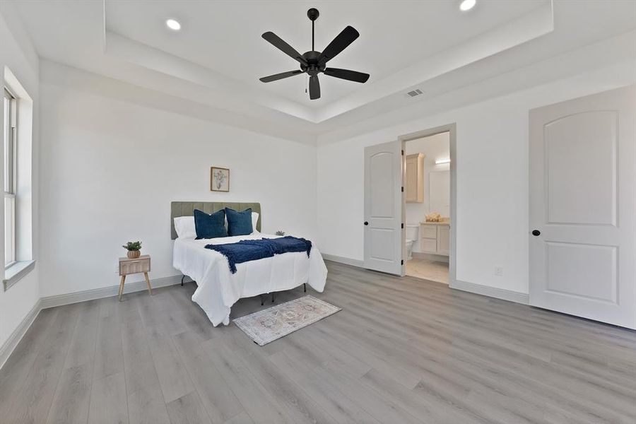 Bedroom with a raised ceiling, light wood-style floors, ceiling fan, and recessed lighting