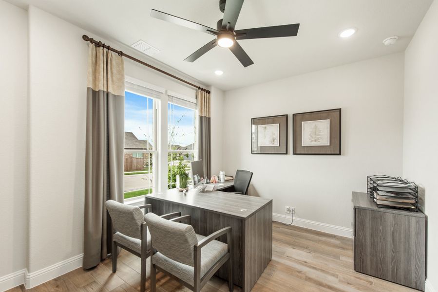 Home office with L-shaped desk, two chairs, ceiling fan, and hardwood floors near a large window