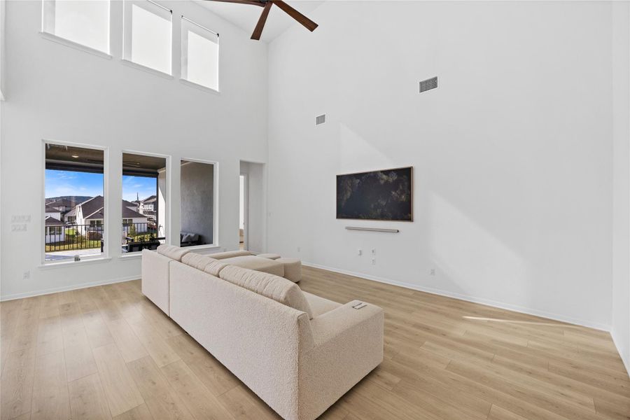 Living room with healthy amount of natural light, a ceiling fan, light wood-style flooring, and a high ceiling