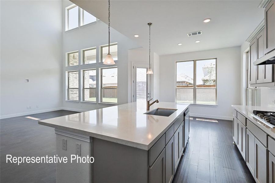 Open concept kitchen featuring a large island with an undermount sink, pendant lighting, and light-toned countertops