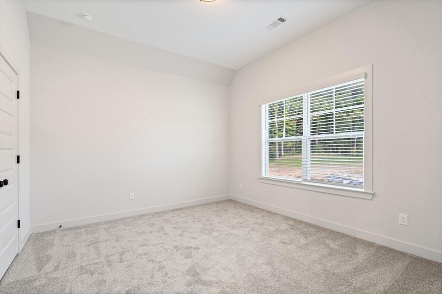 Neutral-toned room featuring a large window with horizontal blinds, light gray carpet, white walls, and a white paneled door with black hardware Neutral-toned room featuring a large window with horizontal blinds, light gray carpet, white walls, and a white paneled door with black hardware