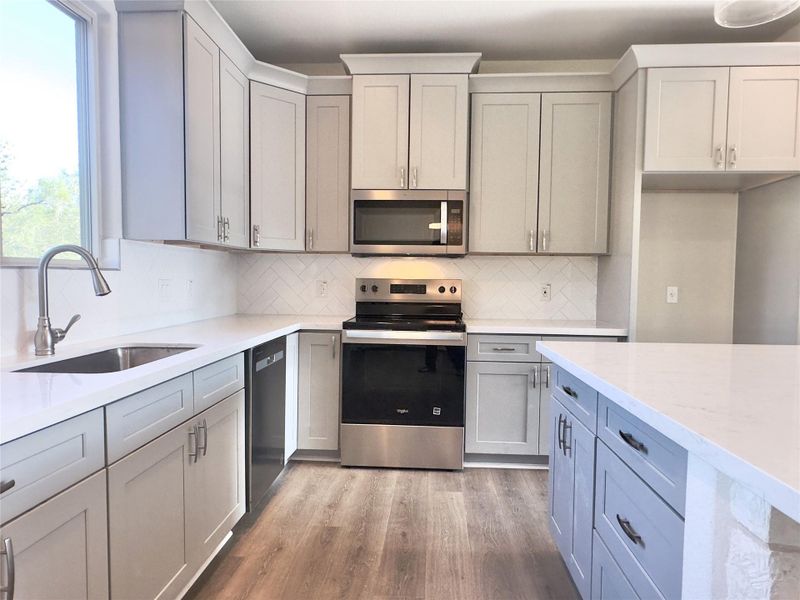 Kitchen with appliances with stainless steel finishes, Luxury Vinyl Plank floors, backsplash, gray cabinets, and light stone countertops Kitchen with appliances with stainless steel finishes, Luxury Vinyl Plank floors, backsplash, gray cabinets, and light stone countertops