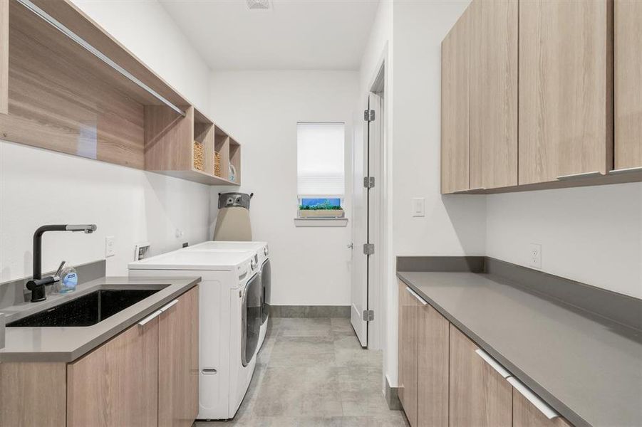 Clothes washing area featuring sink, washing machine and clothes dryer, and cabinets