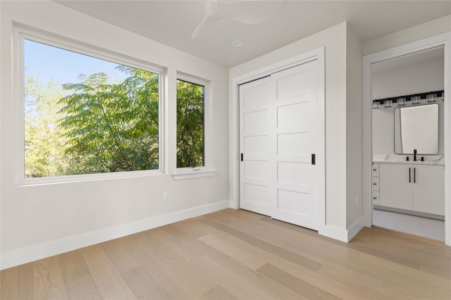 Hardwood flooring and large windows framing lush tree views define this peaceful bedroom.