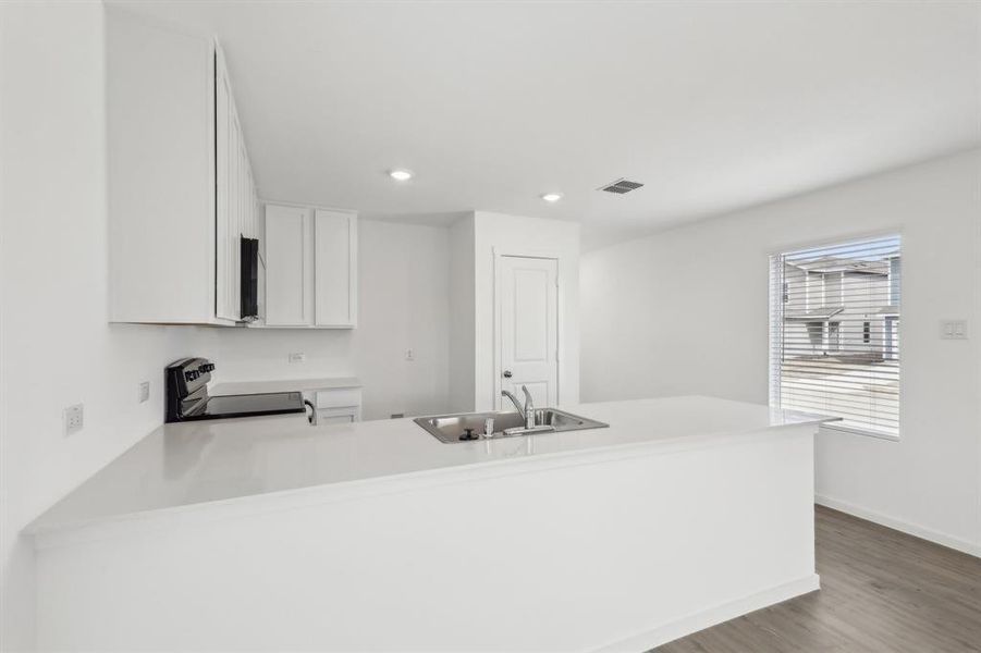 Modern kitchen featuring white cabinetry, light-toned countertops, an integrated stainless steel sink, and wood-finish flooring