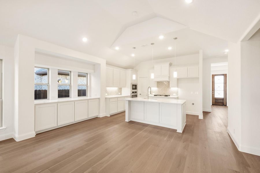 Open kitchen with white cabinets, center island, and hardwood floors under vaulted ceiling Open kitchen with white cabinets, center island, and hardwood floors under vaulted ceiling