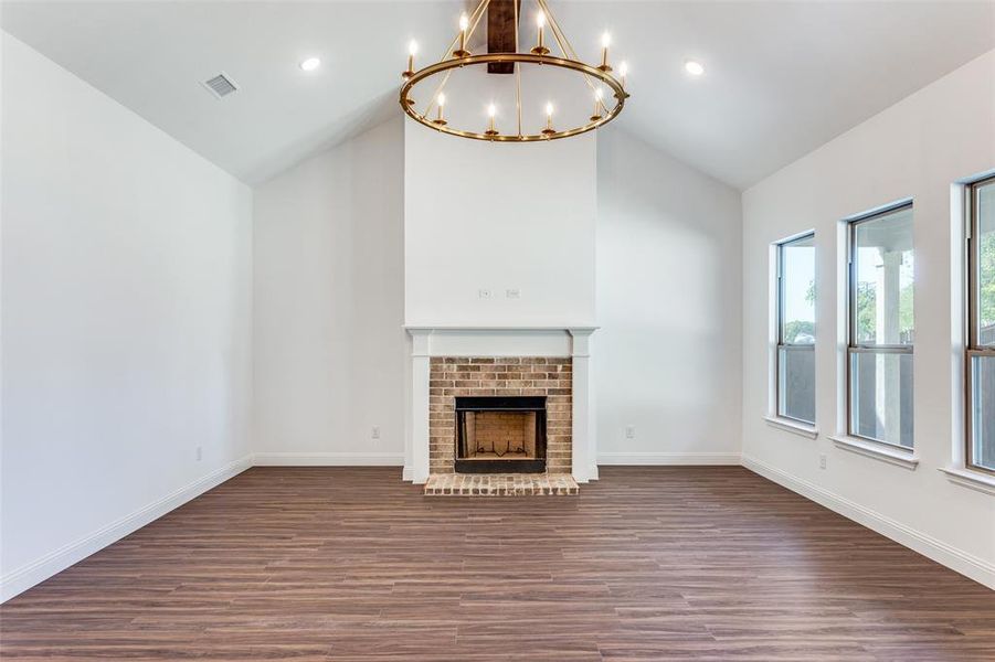 Unfurnished living room featuring high vaulted ceiling, a chandelier, dark hardwood / wood-style floors, and a brick fireplace