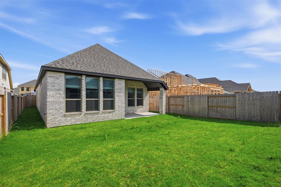 Charming backyard with lush green grass, perfect for outdoor activities, complemented by a modern brick exterior and a cozy patio area.