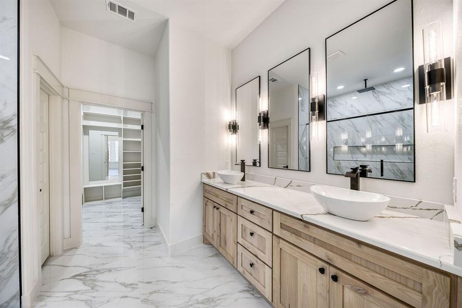Full bath featuring double vanity, a marble finish shower, light marble finish flooring, and a spacious closet