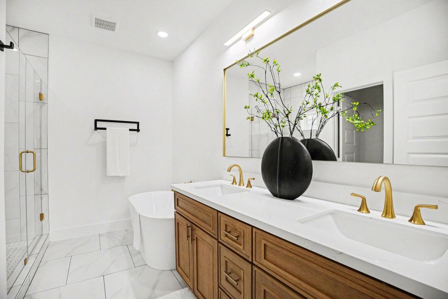 This modern bathroom features a dual-sink vanity with sleek gold fixtures, a large mirror, and elegant cabinetry. A standalone bathtub and a glass-enclosed shower add luxury, complemented by bright lighting and a clean, minimalist design.