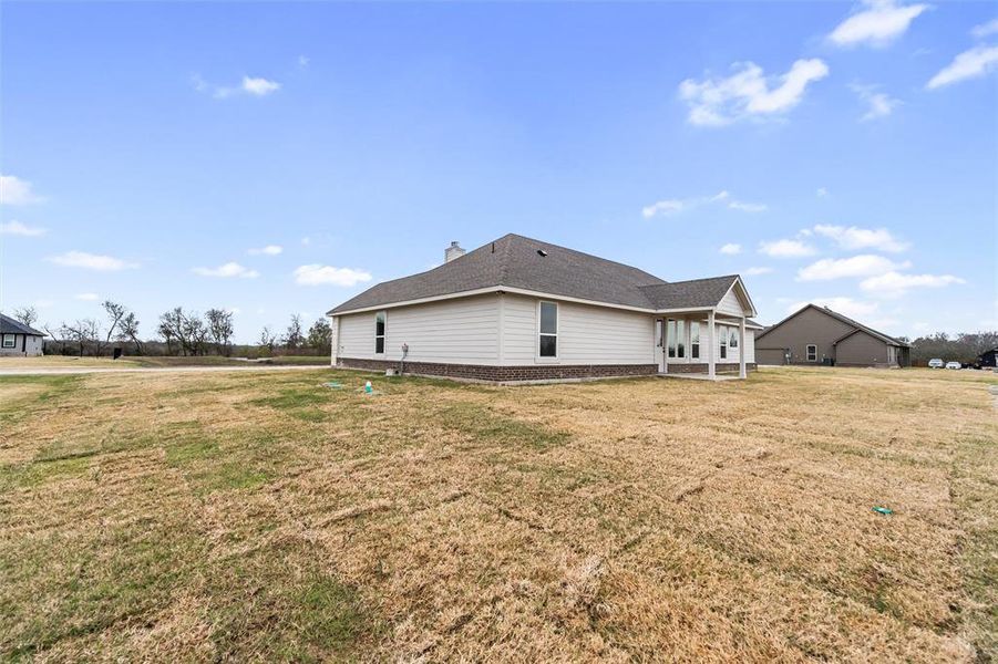 View of side of property with a yard, a patio, and a shingled roof View of side of property with a yard, a patio, and a shingled roof