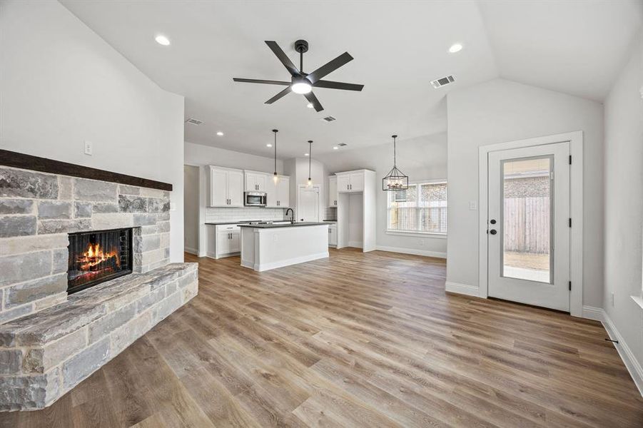 Unfurnished living room featuring a stone fireplace, light wood-type flooring, ceiling fan, a chandelier, and recessed lighting