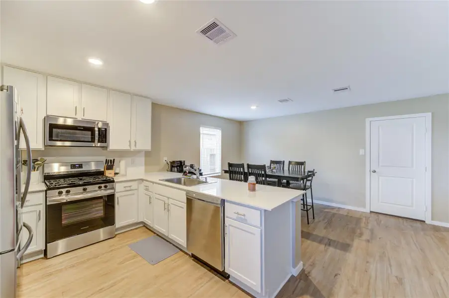 This kitchen features modern stainless steel appliances, white cabinetry, and a spacious island with seating. The open layout connects to a dining area with vinyl plank flooring and ample natural light.