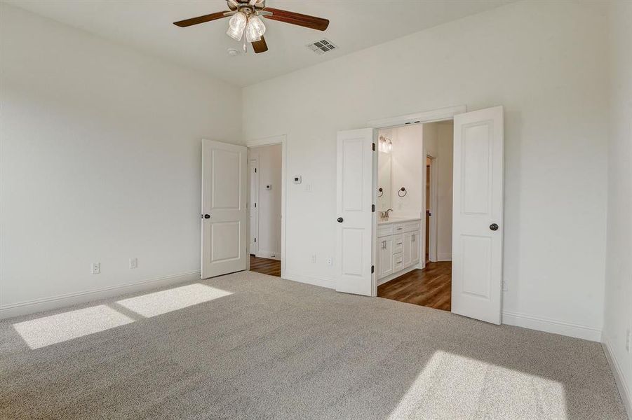 Unfurnished bedroom with ceiling fan, connected bathroom, sink, and dark colored carpet