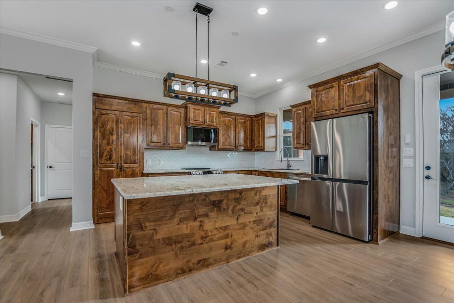 Kitchen featuring stainless steel appliances, a kitchen island, light stone countertops, recessed lighting, and ornamental molding