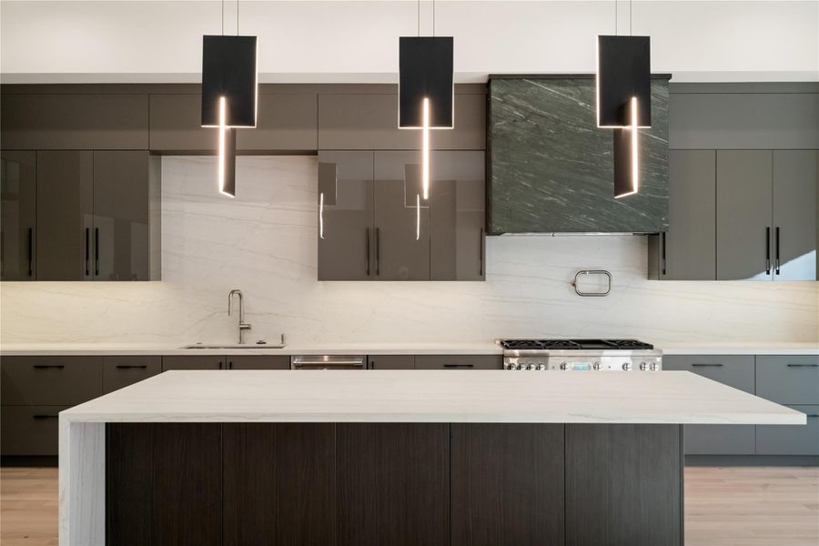 Sleek modern kitchen featuring dark cabinetry, a large marble island, and contemporary pendant lights. The backsplash and countertop provide a clean, elegant look, with a high-end stove and hood for a sophisticated touch.