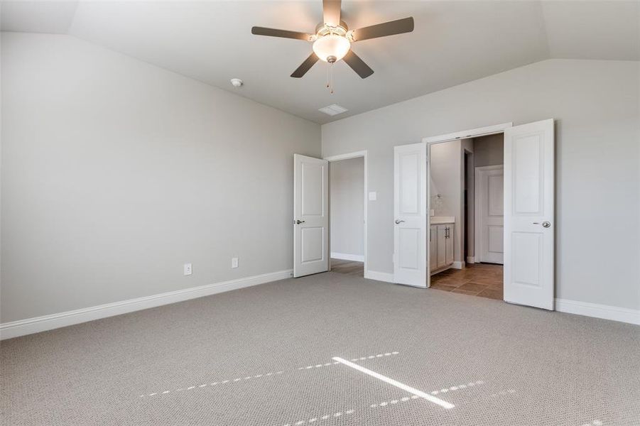 Unfurnished bedroom featuring light colored carpet, lofted ceiling, ensuite bath, and a ceiling fan