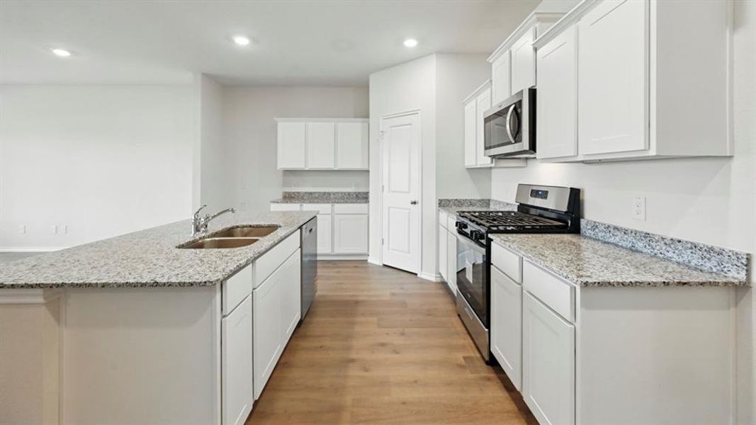 Kitchen featuring appliances with stainless steel finishes, light stone counters, white cabinetry, a center island with sink, and dark wood-style floors