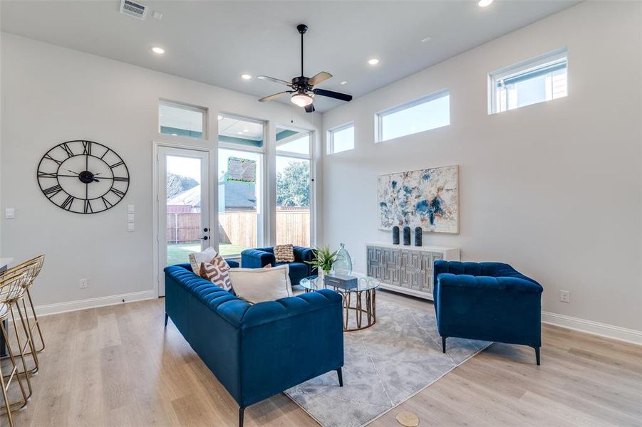 Living room featuring ceiling fan, a high ceiling, and light wood-type flooring