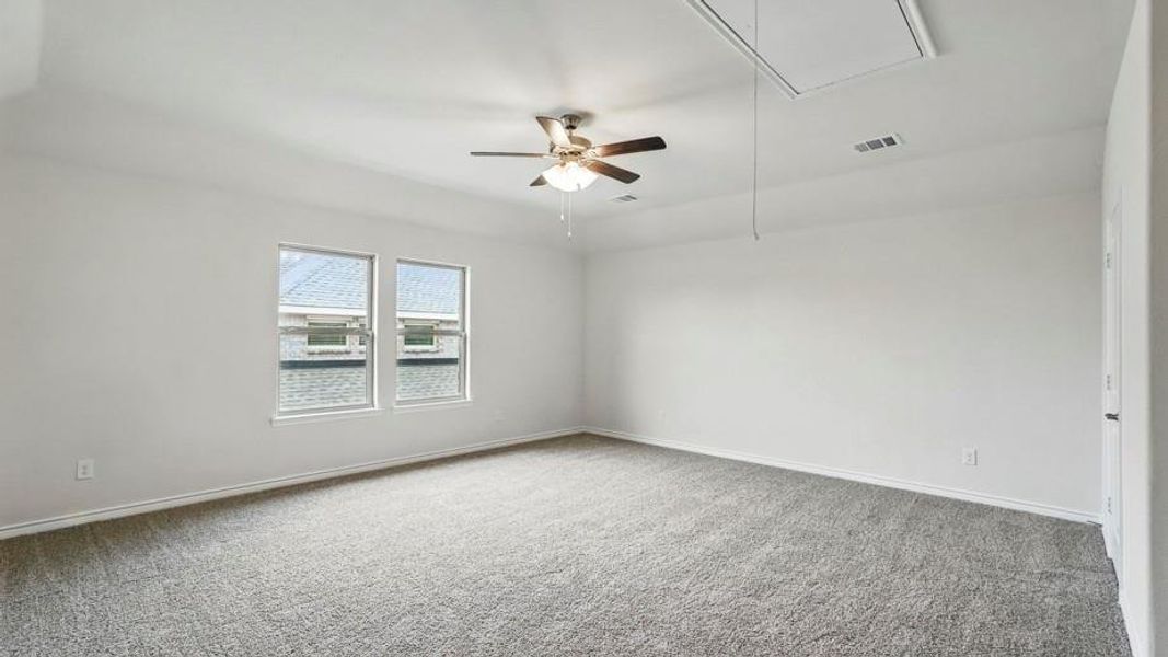 Spacious room with plush gray carpeting, two large windows, a ceiling fan with light fixture, and an attic access panel