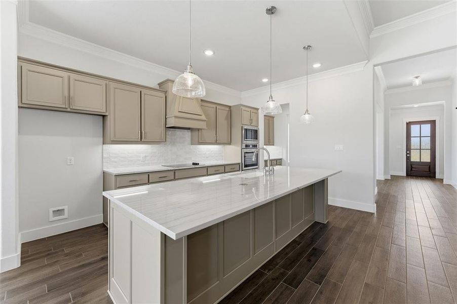 Kitchen featuring wood finish floors, an island with sink, decorative backsplash, light stone countertops, and hanging light fixtures