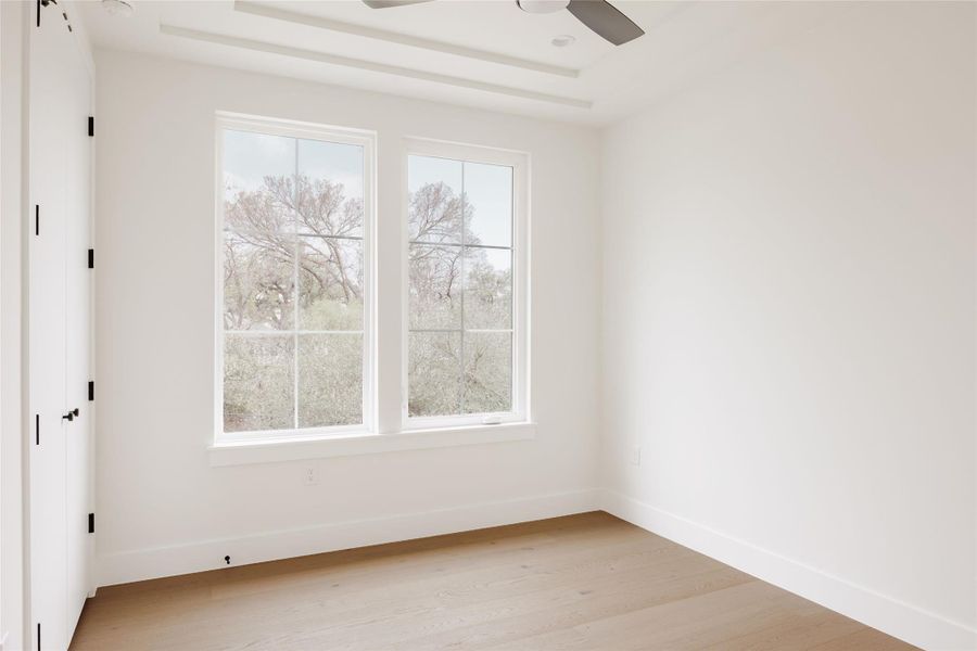 Spare room featuring light wood-style flooring, ceiling fan, and a tray ceiling