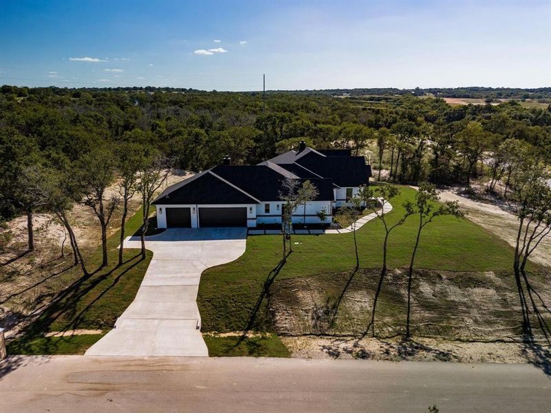 View of front of house with a wooded view, a garage, a front lawn, and concrete driveway